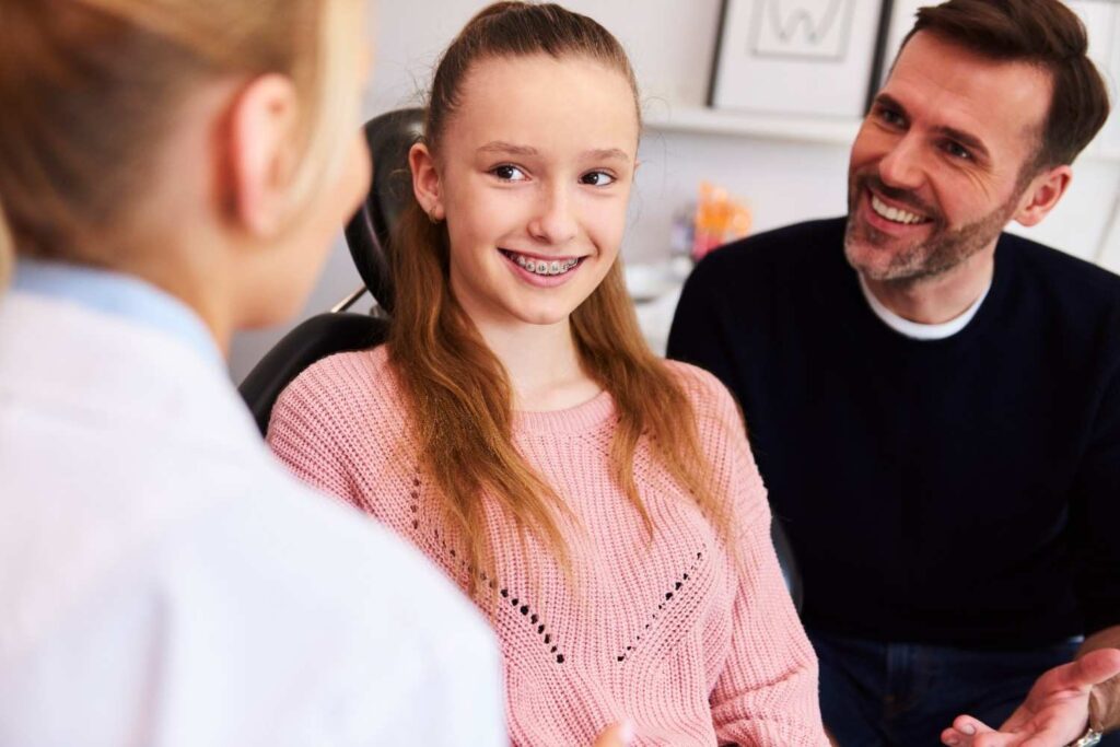 Teen with braces smiling during a dental visit with a parent.